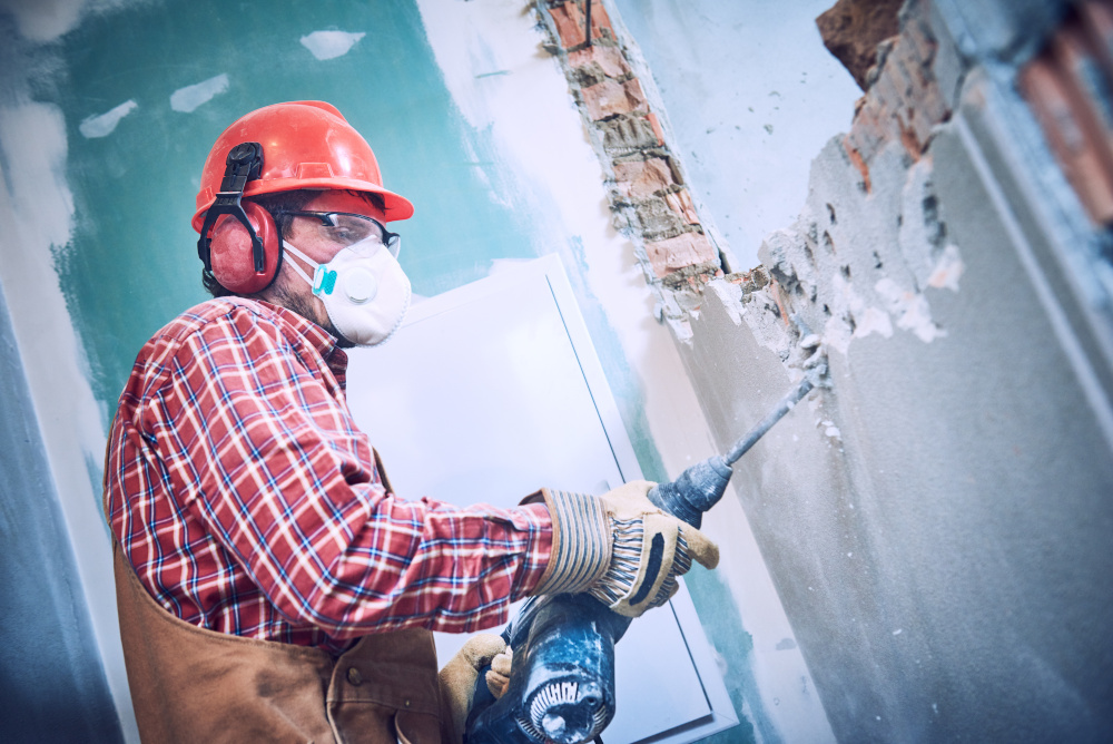 Worker with personal protection equipment and demolition hammer breaking in an interior brick wall