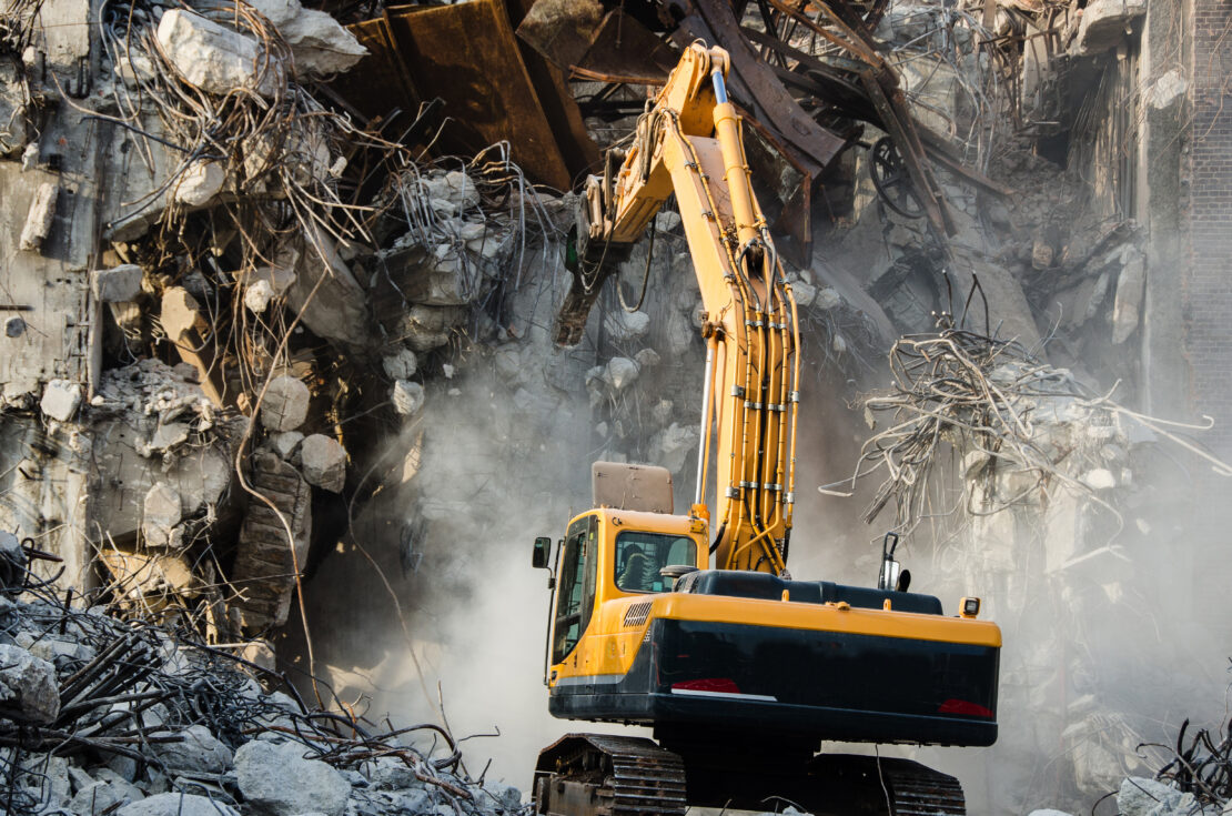 An excavator uses a crane to demolish an old industrial building. 