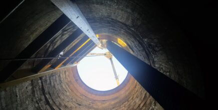 An upward shot of the inside of a manhole, showing a ladder and an extended retrieval winch
