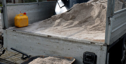 silica sand is in the bed of a truck. Just underneath the truck bed is a wheelbarrow with more silica sand in it.